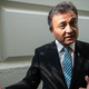 Dolkun Isa stands with his back to a white brick wall, gesturing to his right with his hands.